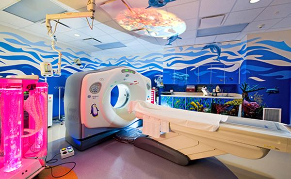 A CT imaging room has colorful decals on the wall with a calming effect for children