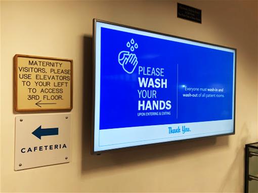 An indoor screen shows a digital sign reminding viewers to wash their hands
