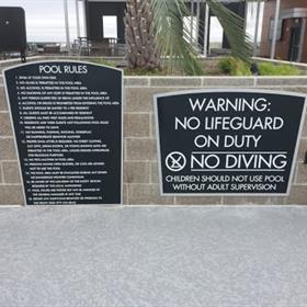 Outside of a pool are signs for safety and rules